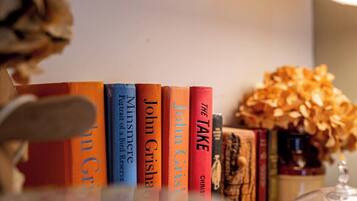 Une rangée de livres sur une étagère, avec un vase de fleurs séchées en arrière-plan.