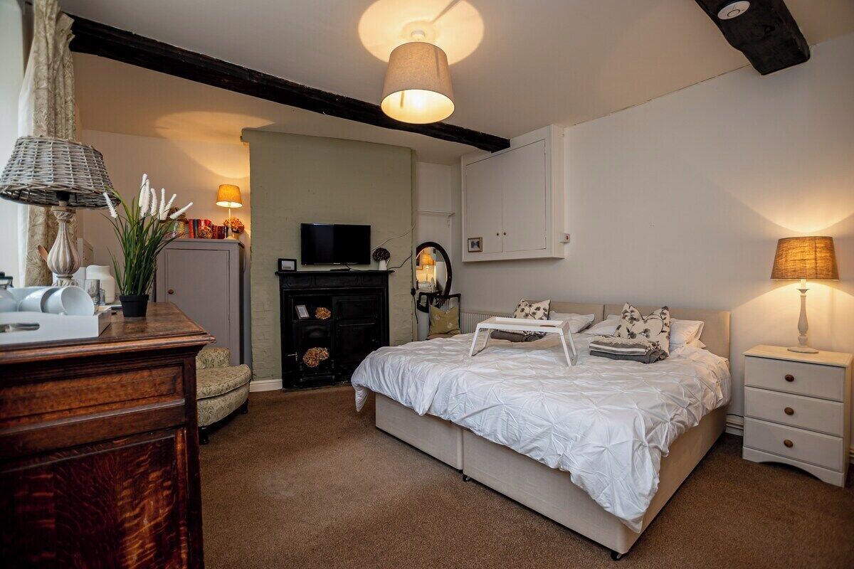 Une chambre à coucher comprenant un lit, des tables de chevet, une commode, un téléviseur et une cheminée.