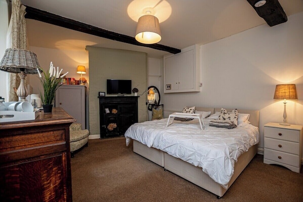 A bedroom with a bed, bedside tables, a dresser, a television, and a fireplace.