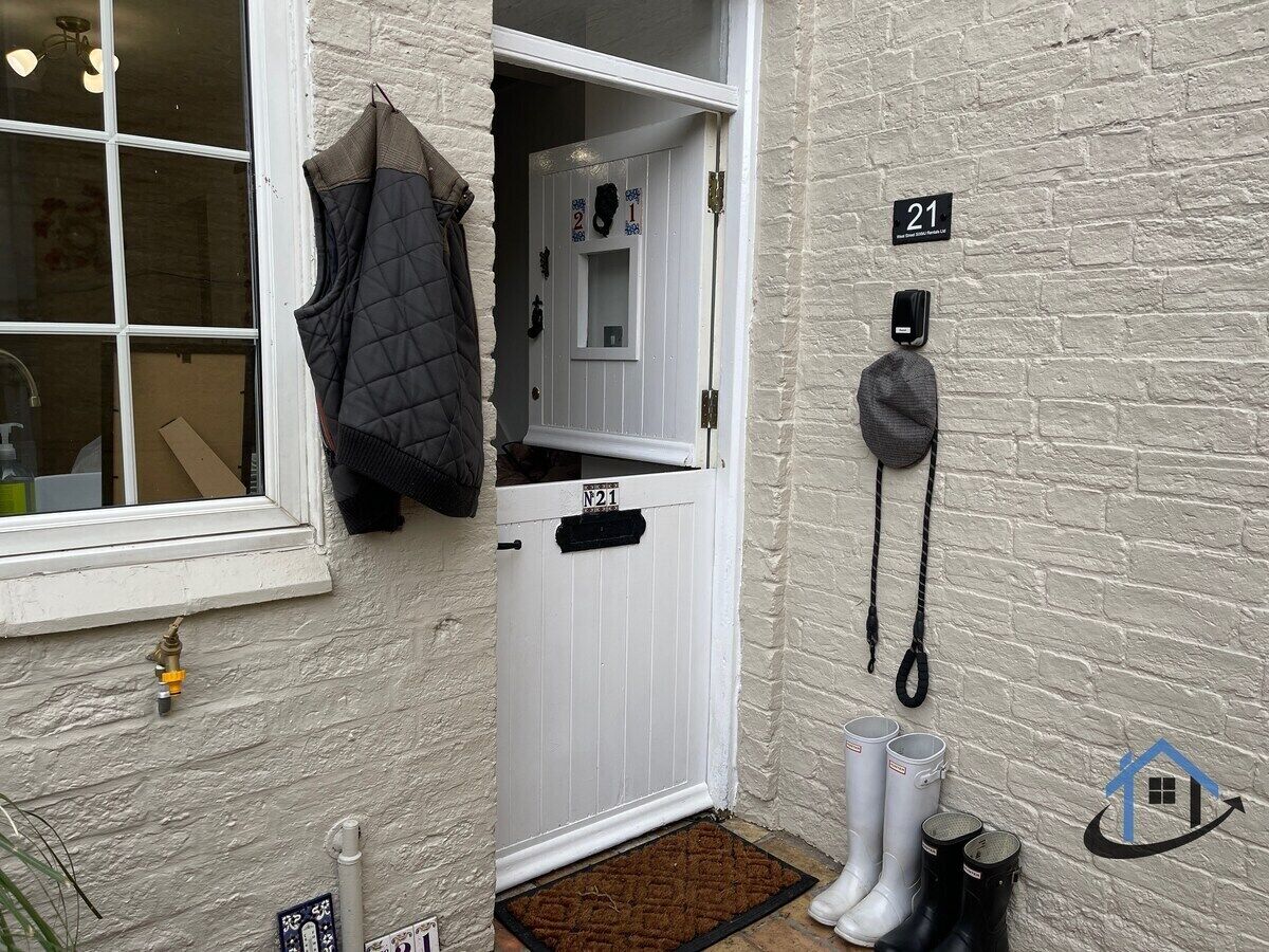 A white door with a number plate, a coat hanging on the wall, and a doorbell.