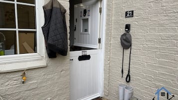 A white door with a number plate, a coat hanging on the wall, and a doorbell.