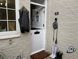 A white door with a number plate, a coat hanging on the wall, and a doorbell. - Petham Cottage 2 bed sleeps 6 (Stanwick)