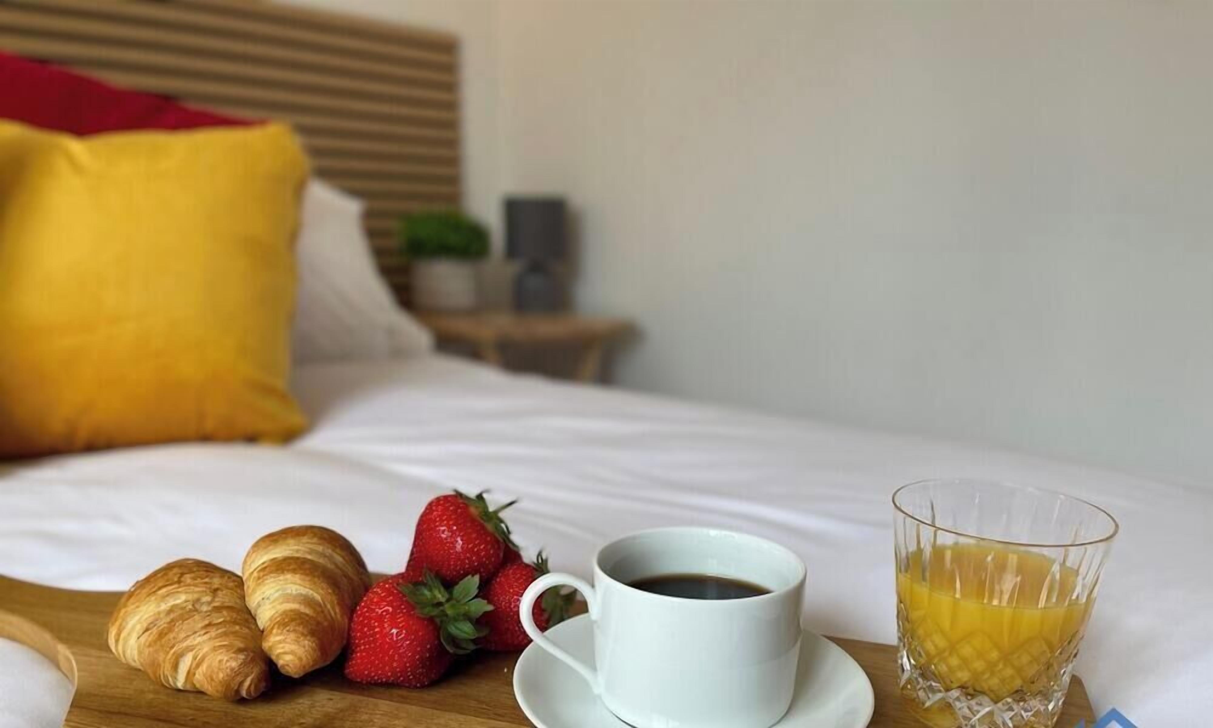 A neatly made bed with a white duvet, a wooden headboard, and a bedside table with a lamp and a small plant.