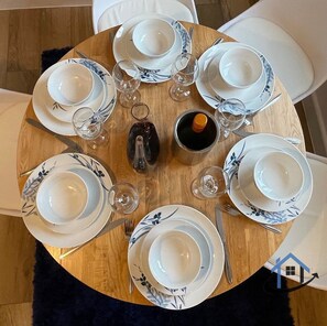 Mesa de jantar redonda com pratos brancos e estampas florais azuis, acompanhada de copos de vinho e talheres.
