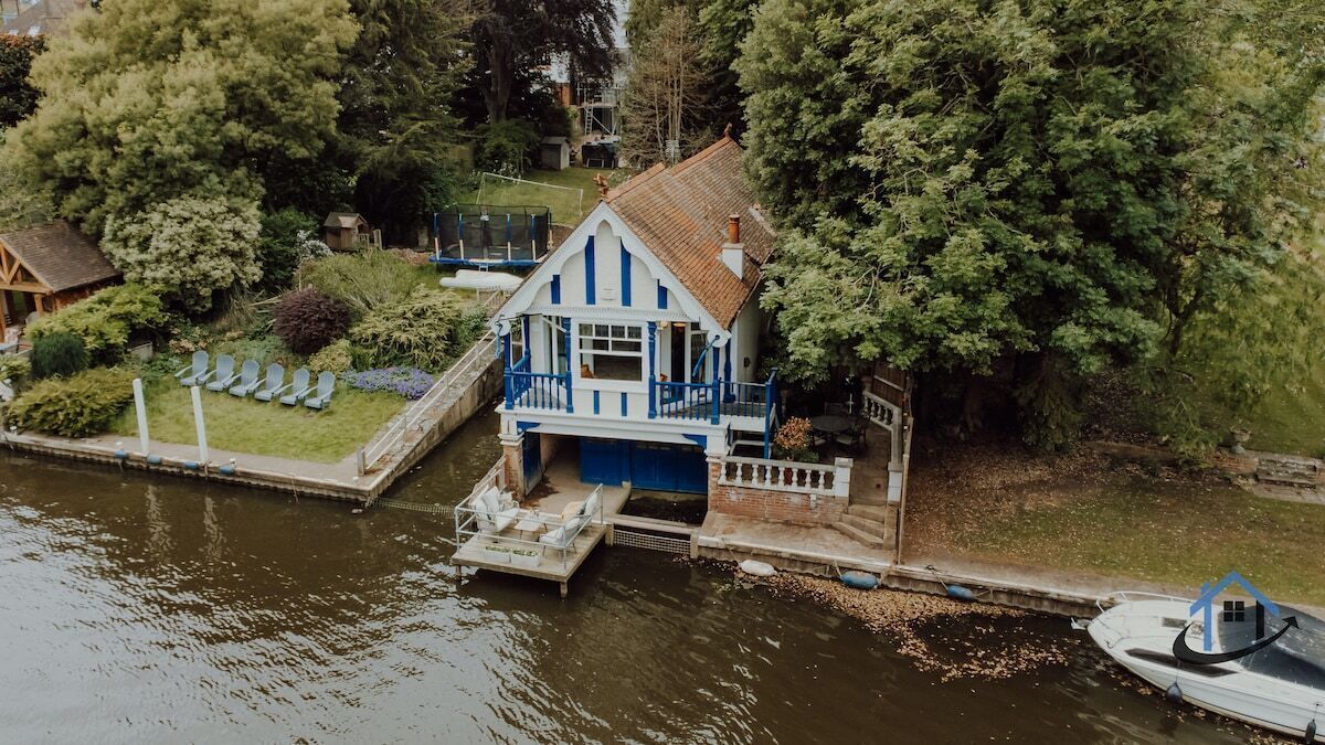 A house with a dock extending into a body of water, surrounded by trees and greenery.