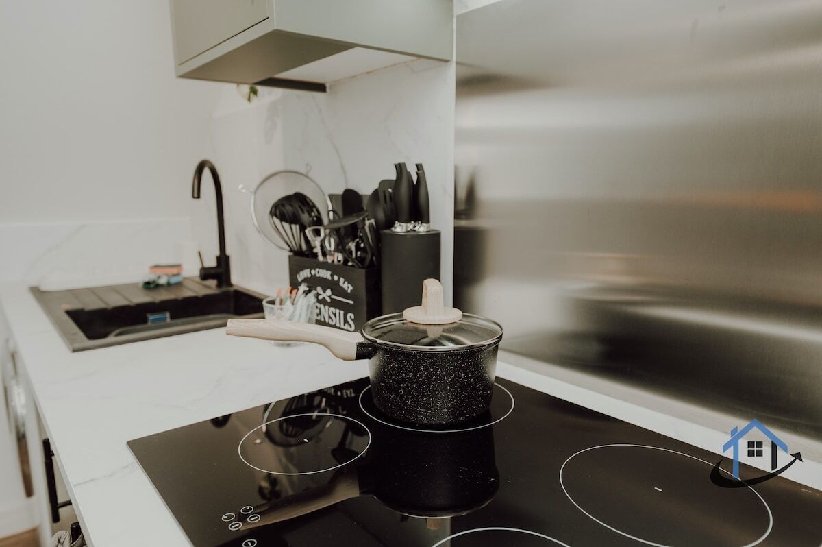 Uma cozinha com um fogão por indução preto, uma panela sobre ele e um conjunto de utensílios de cozinha em cima do balcão.