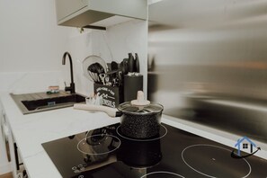 Uma cozinha com um fogão por indução preto, uma panela sobre ele e um conjunto de utensílios de cozinha em cima do balcão.