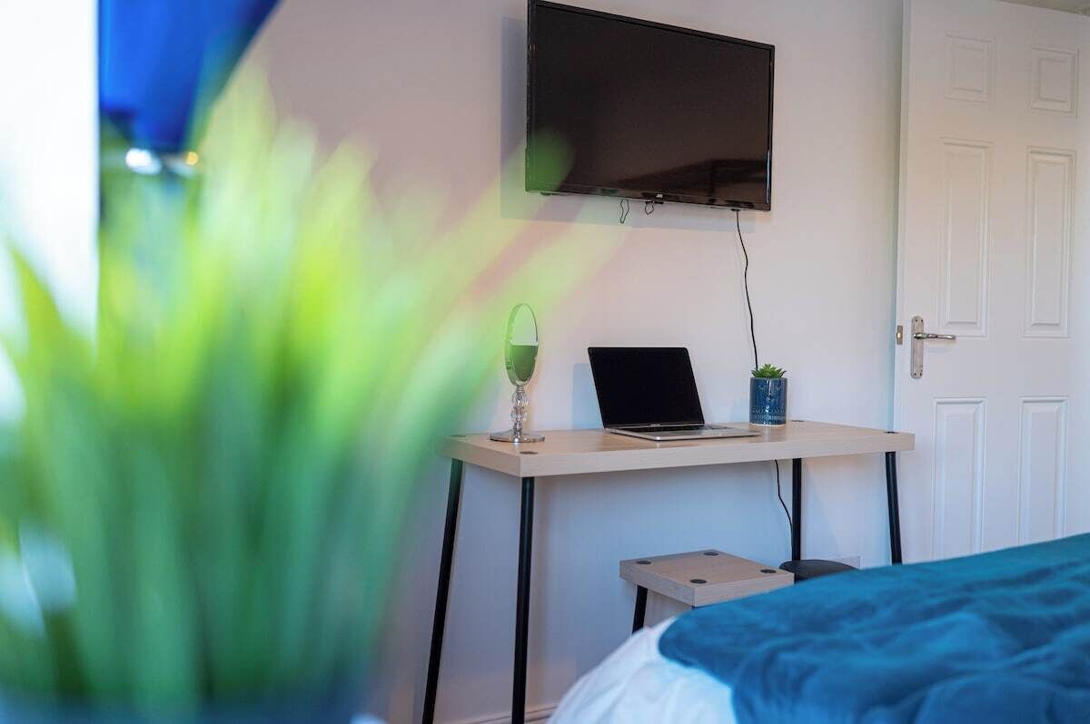 Una camera da letto con un letto, una scrivania con un portatile, una televisione a parete e una porta.