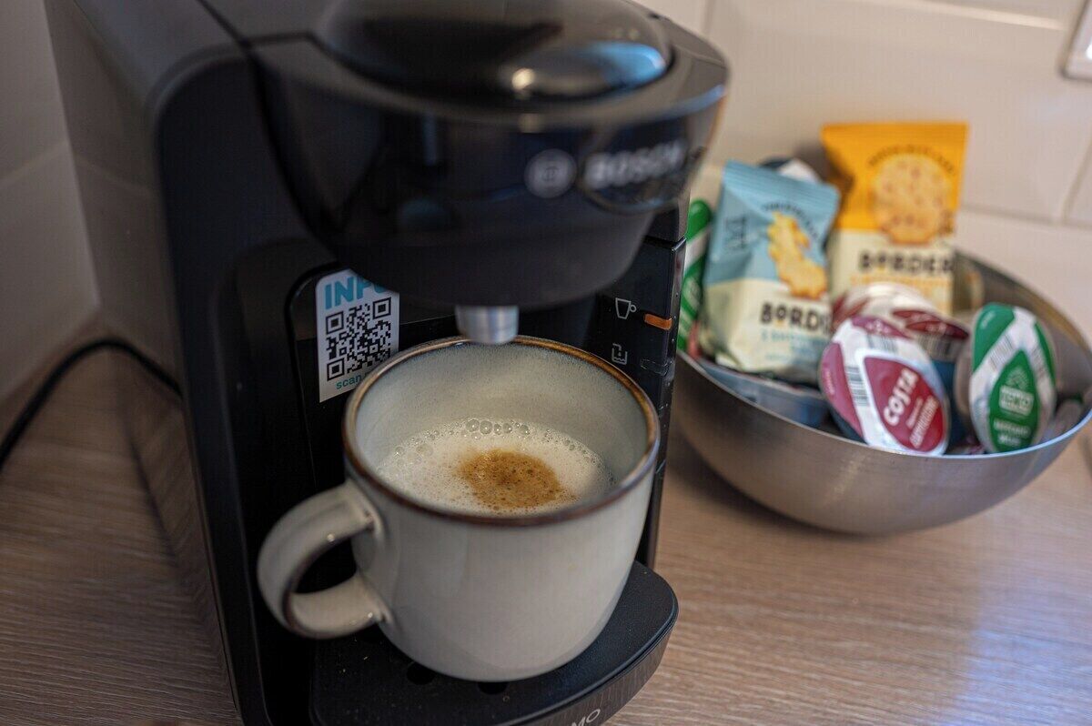 A coffee maker dispensing coffee into a cup, with a bowl of snacks beside it.