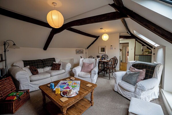 A cozy loft-style living room with white furniture, a wooden coffee table, and a dining area with a table and chairs.