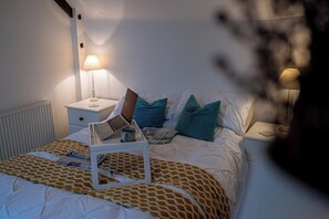 A neatly made bed with a patterned bedspread, a bedside table with a lamp, and a tray with a laptop and a cup.