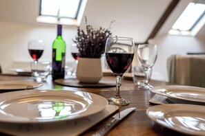 A dining table set with plates, cutlery, and wine glasses, with a bottle of wine and a vase of flowers in the background.