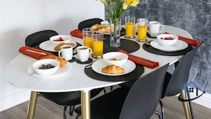 A breakfast table set with croissants, fruit, coffee, and juice, with a vase of flowers in the center. - Bluebell House, sleeps 7, parking x2, garden (Corby)