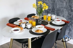 Ett frukostbord dukat med croissanter, frukt, kaffe och juice, och en vas med blommor i mitten.