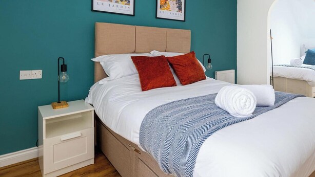 A bedroom with a bed, nightstands, a lamp, and two framed artworks on the wall. - Bluebell House, sleeps 7, parking x2, garden (Corby)