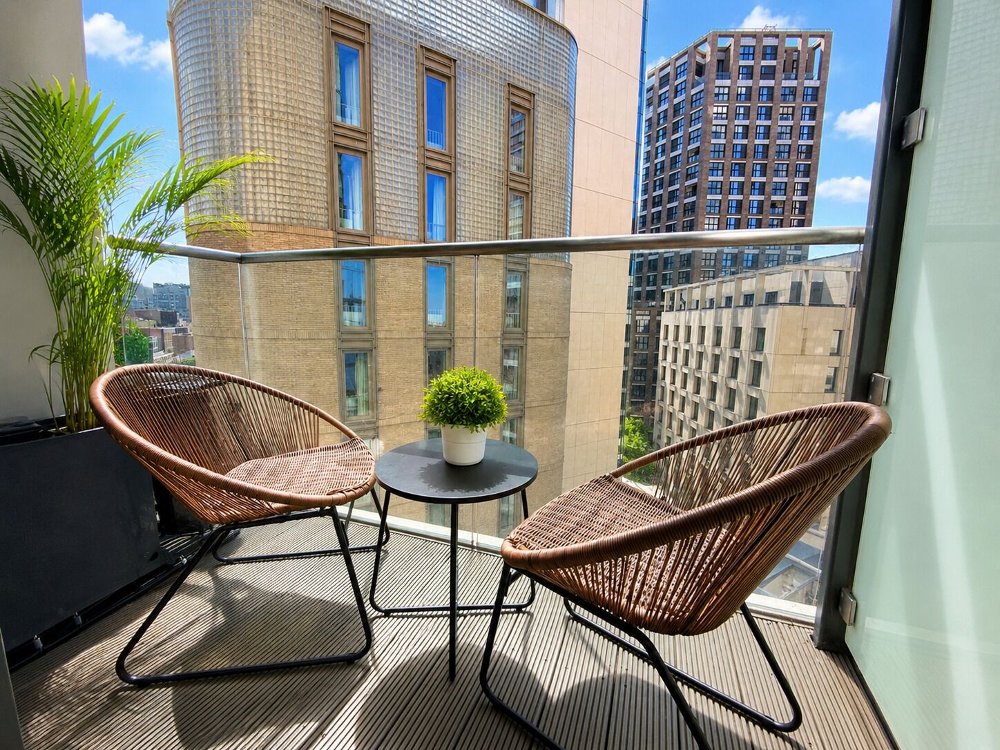 Ein Balkon mit zwei Korbstühlen, einem kleinen Tisch und einem Blumentopf.