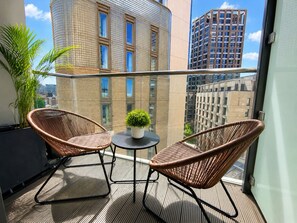 A balcony with two wicker chairs, a small table, and a potted plant. - Luxury City View AC Balcony Rooftop Panoramic - Fast Wi-fi, near Sky Garden (London)