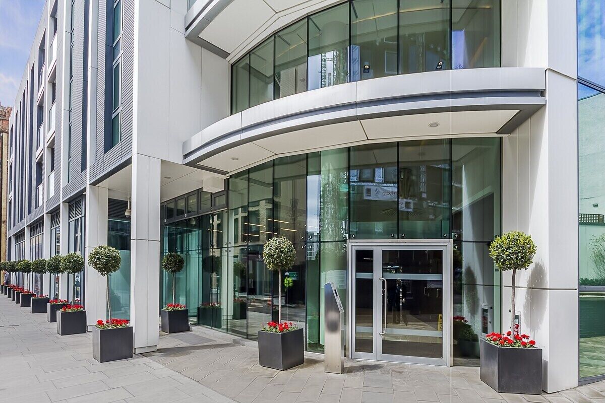 Ein moderner Hotelzugang mit geschwungener Fassade, großen Glastüren und Topfpflanzen.