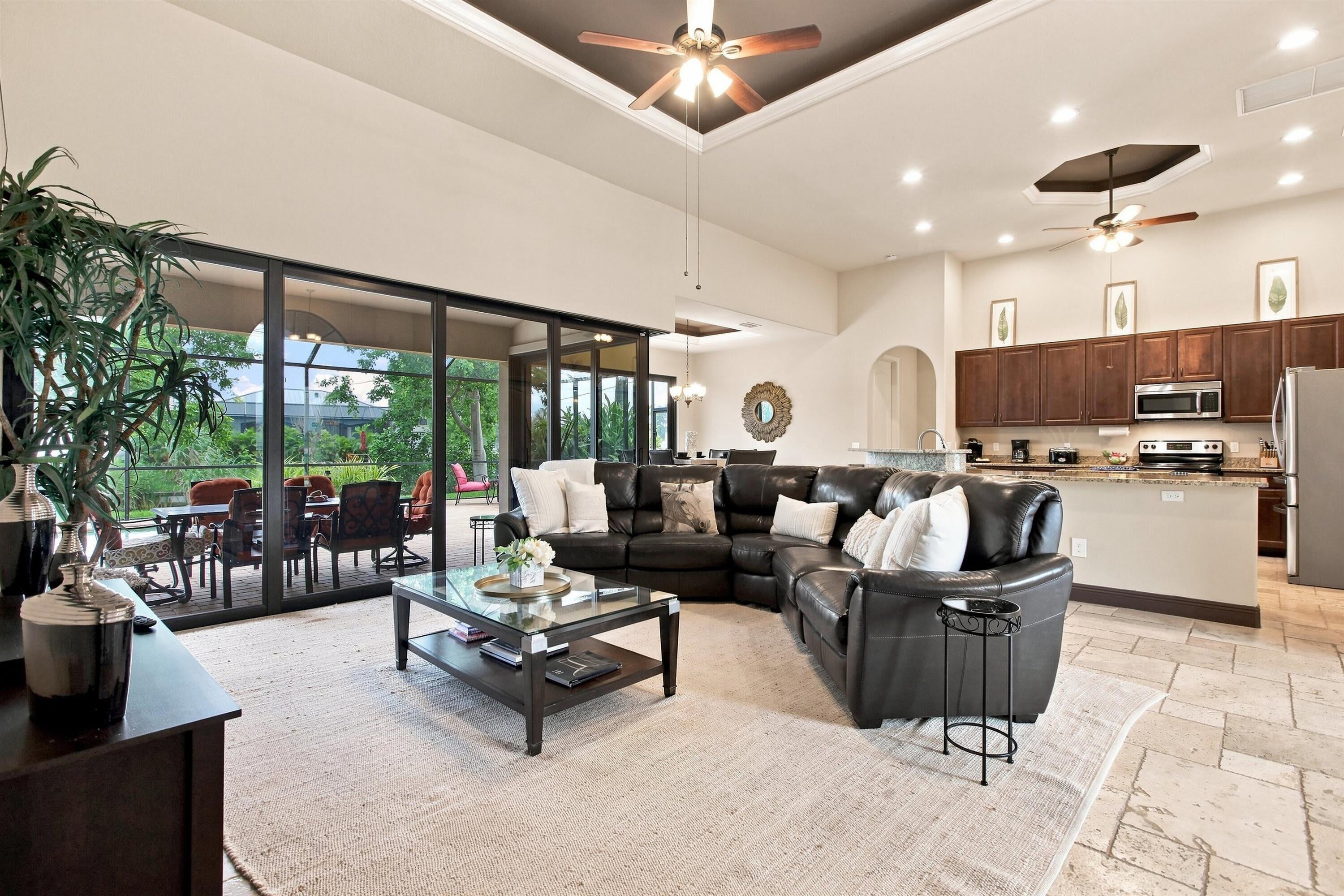 A spacious living area with a leather sofa, a glass coffee table, and a view through large sliding glass doors to an outdoor patio.