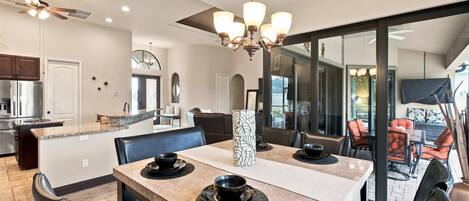 A modern dining area with a large table, chairs, and a chandelier.