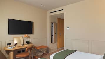Une chambre d’hôtel équipée d’un bureau, de deux chaises, d’un lit, d’une télévision et d’une armoire.
