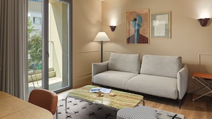 Quarto de hotel moderno com sofá, mesa de centro, luminária e obras de arte nas paredes.