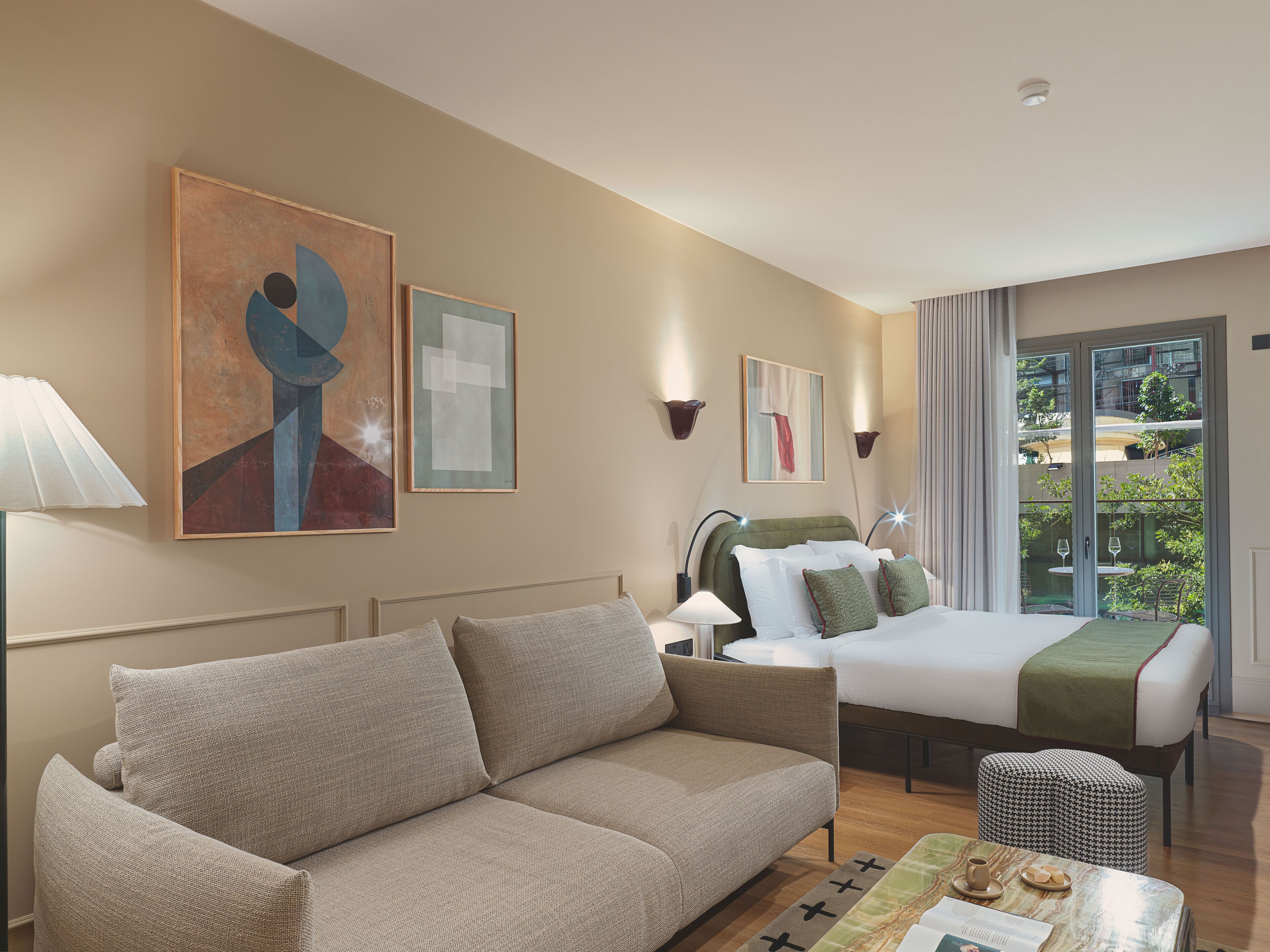 Une chambre d’hôtel avec un canapé, un lit doté d’une tête de lit verte, une petite table avec un plateau, et des œuvres d’art accrochées aux murs.