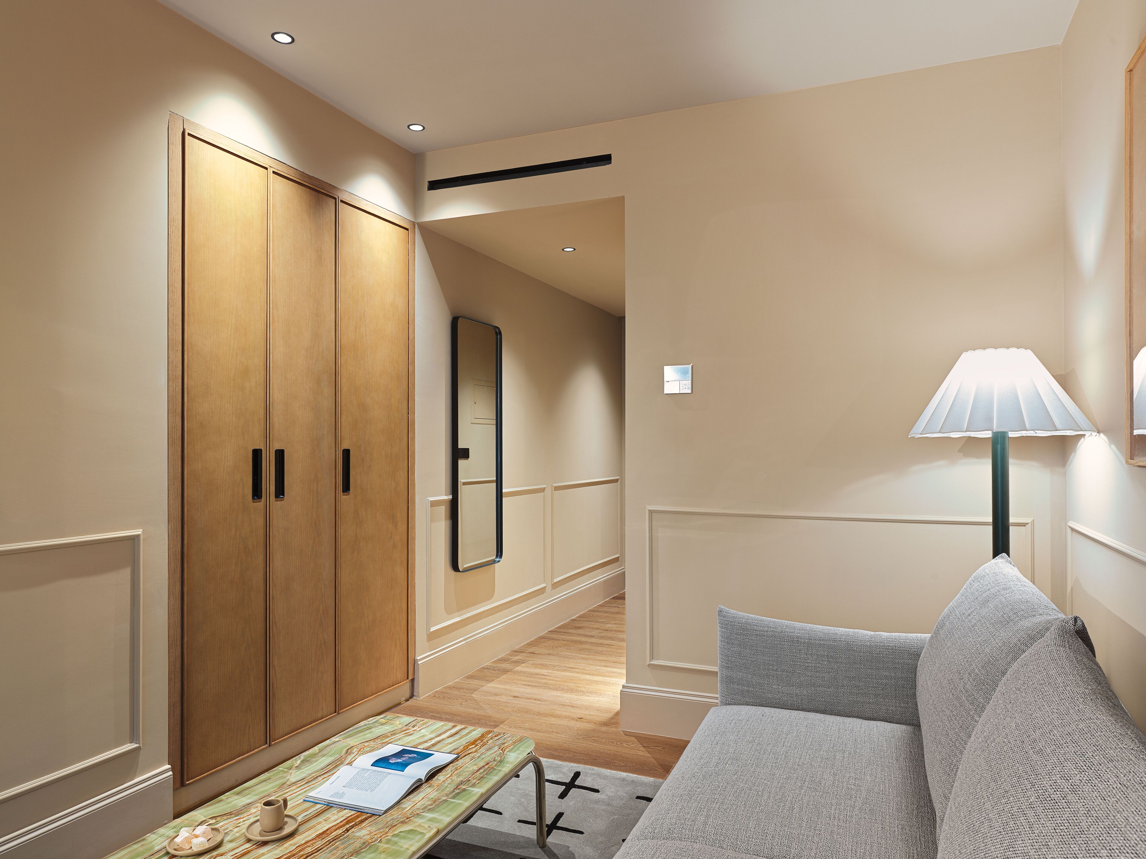 Une chambre d’hôtel avec une armoire en bois, un miroir, un canapé et une table sur laquelle se trouvent un magazine et une tasse.