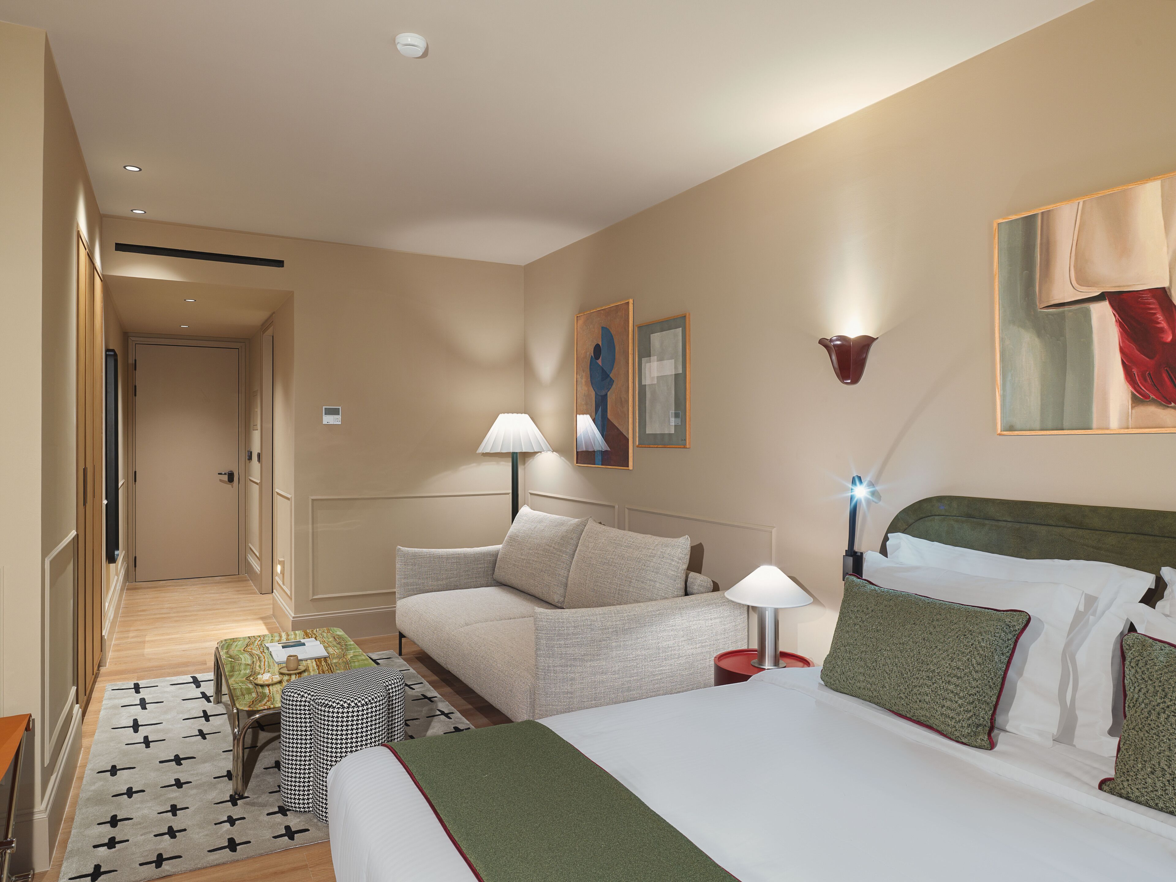 Habitación de hotel con cama, sofá, una mesita, lámpara y obras de arte en las paredes.