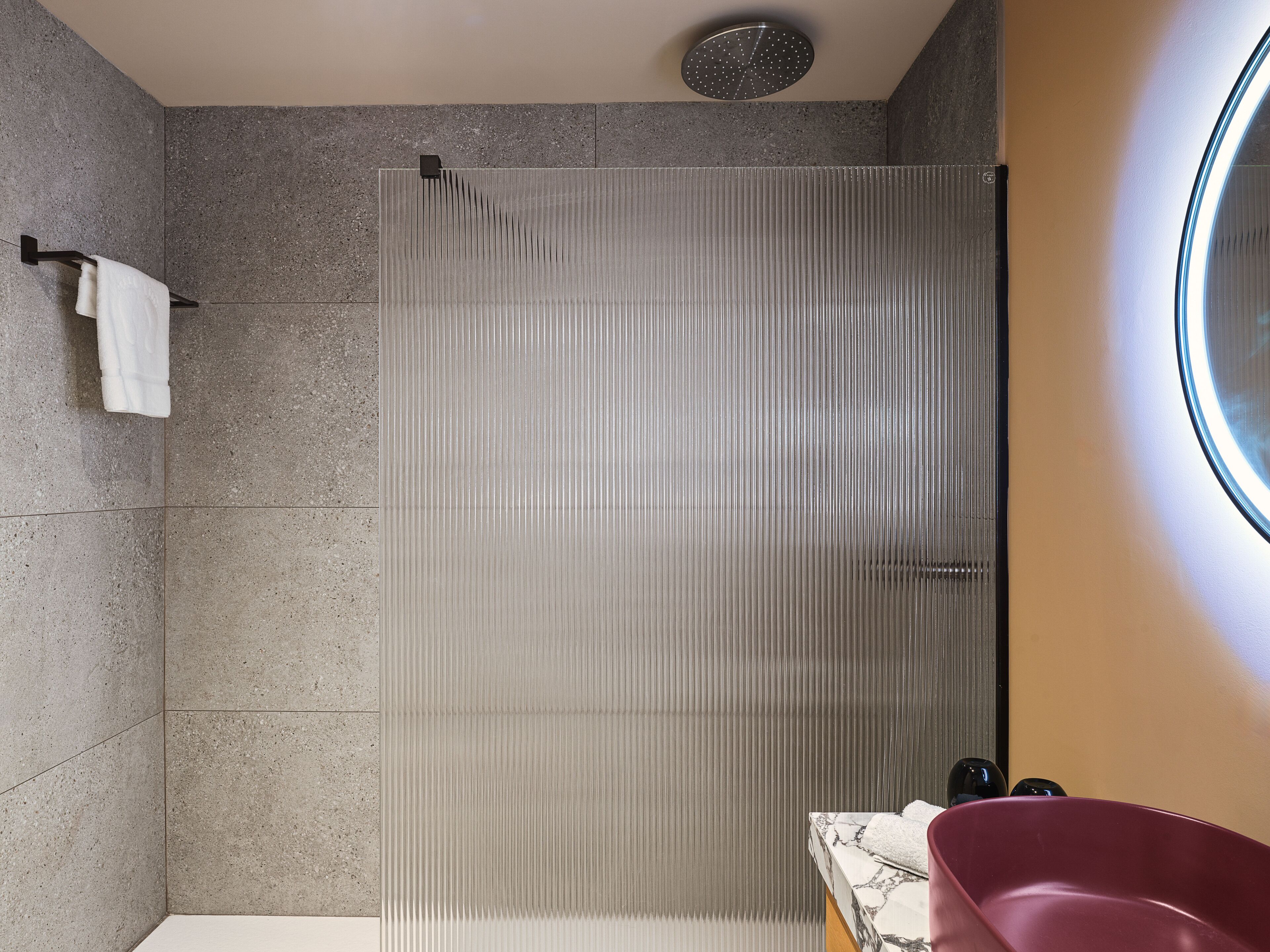 Une salle de bain moderne avec une douche, un comptoir en marbre et une baignoire rouge.