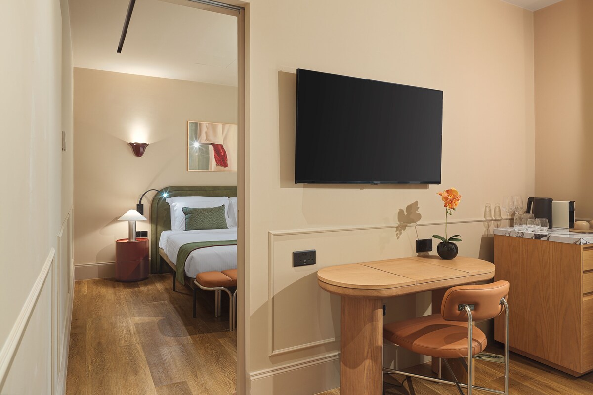 A hotel room with a bed, a desk, a chair, a television, and a small table with glasses.