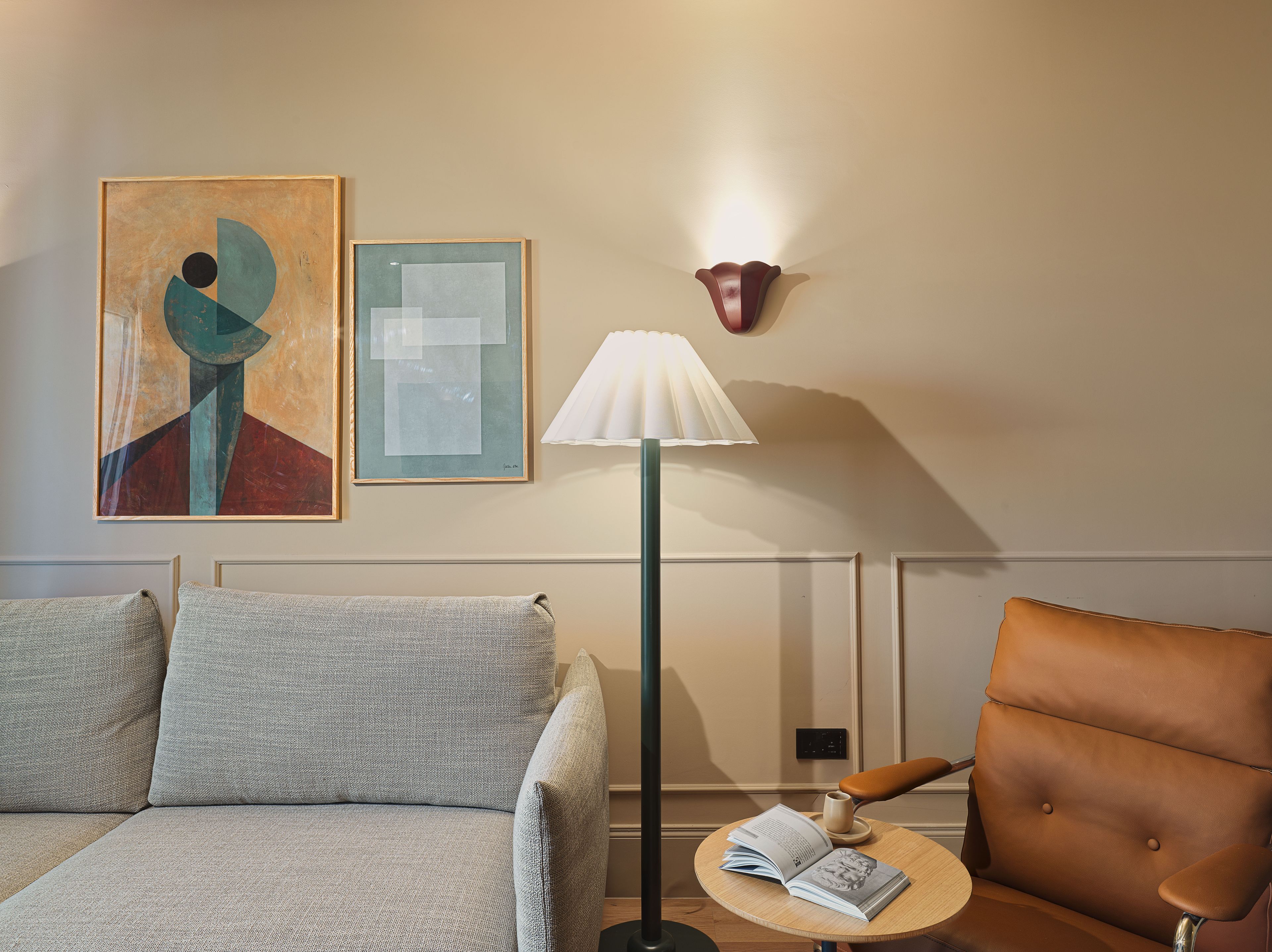 A living room with a sofa, a chair, a lamp, and two artworks on the wall.