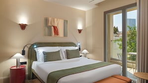 Quarto de hotel com cama, abajures, um banco, uma pintura e vista para a cidade.