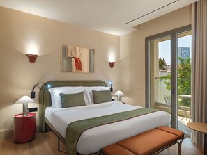 A hotel room with a bed, bedside lamps, a bench, a painting, and a view of the city. - Leonardo Boutique Hotel Venetian Nicosia (Nicosia)