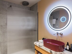 A bathroom with a glass shower enclosure, a round mirror with a light, and a red sink with a marble countertop. - Leonardo Boutique Hotel Venetian Nicosia (Nicosia)
