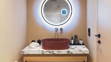 Un baño con un espejo redondo, un lavabo rojo y una encimera de mármol.