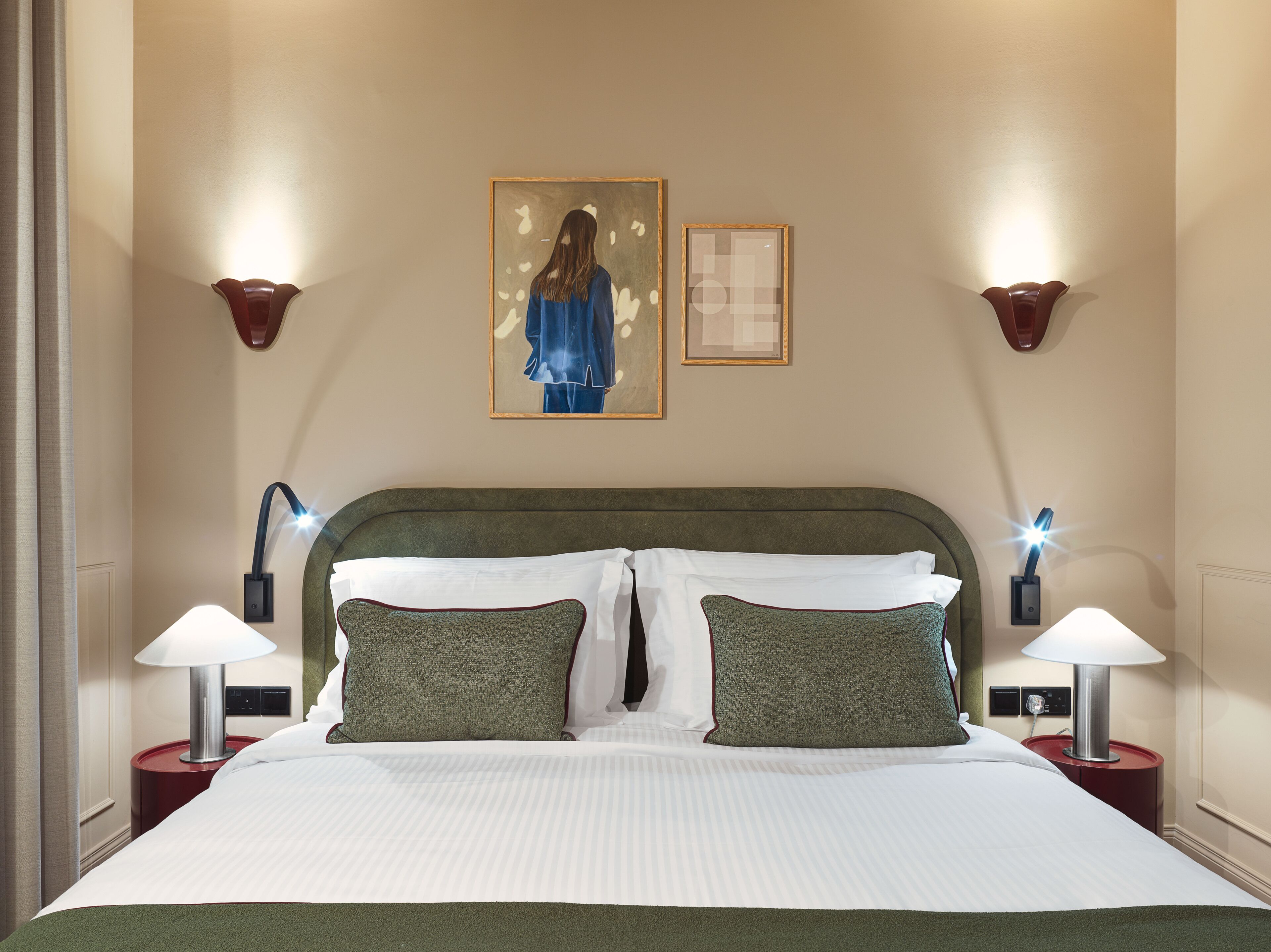 A hotel room with a large bed, two wall-mounted lamps, and two framed artworks on the wall.