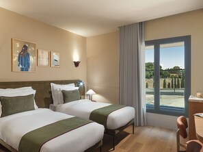 A hotel room with two beds, a desk, a chair, a window with a view, and artwork on the wall. - Leonardo Boutique Hotel Venetian Nicosia (Nicosia)