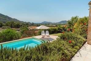 Una piscina amb dues cadires i una ombrelles, envoltada de vegetació i amb vista a les muntanyes.
