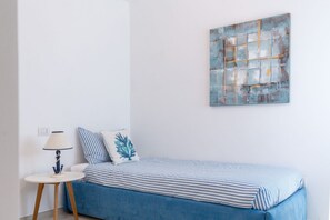 Ein Schlafzimmer mit einem Einzelbett, einem Nachttisch mit Lampe und einem an der Wand hängenden abstrakten Gemälde.