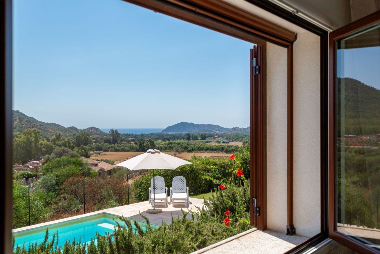 A poolside area with two chairs and an umbrella, overlooking a scenic landscape with hills and a clear sky.