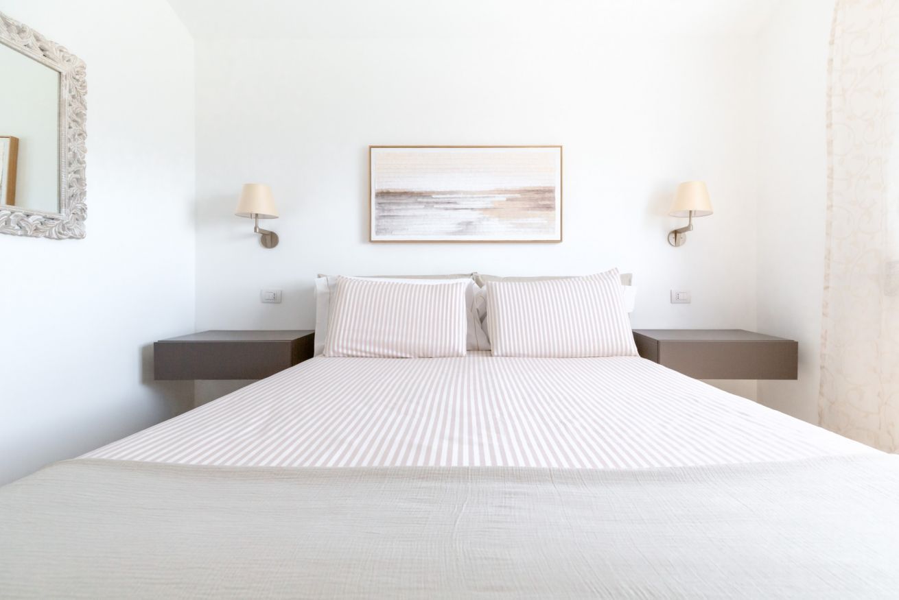 A hotel room with a large bed, two bedside tables, a wall-mounted lamp, and a framed picture on the wall.