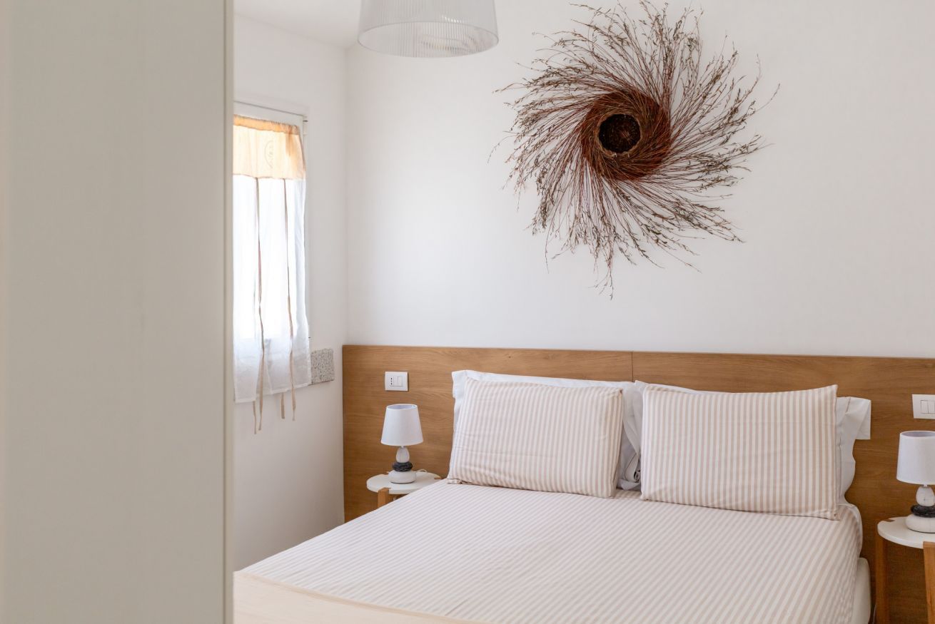 Een slaapkamer met een bed, twee bedlampen, een raam met gordijnen en een decoratief object aan de muur.