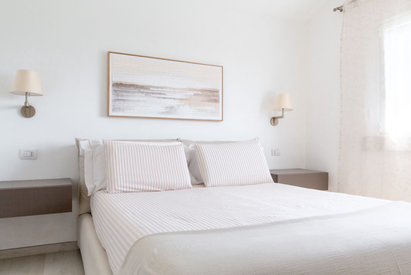 A bedroom with a bed, two bedside tables, a wall-mounted light fixture, and a framed artwork.