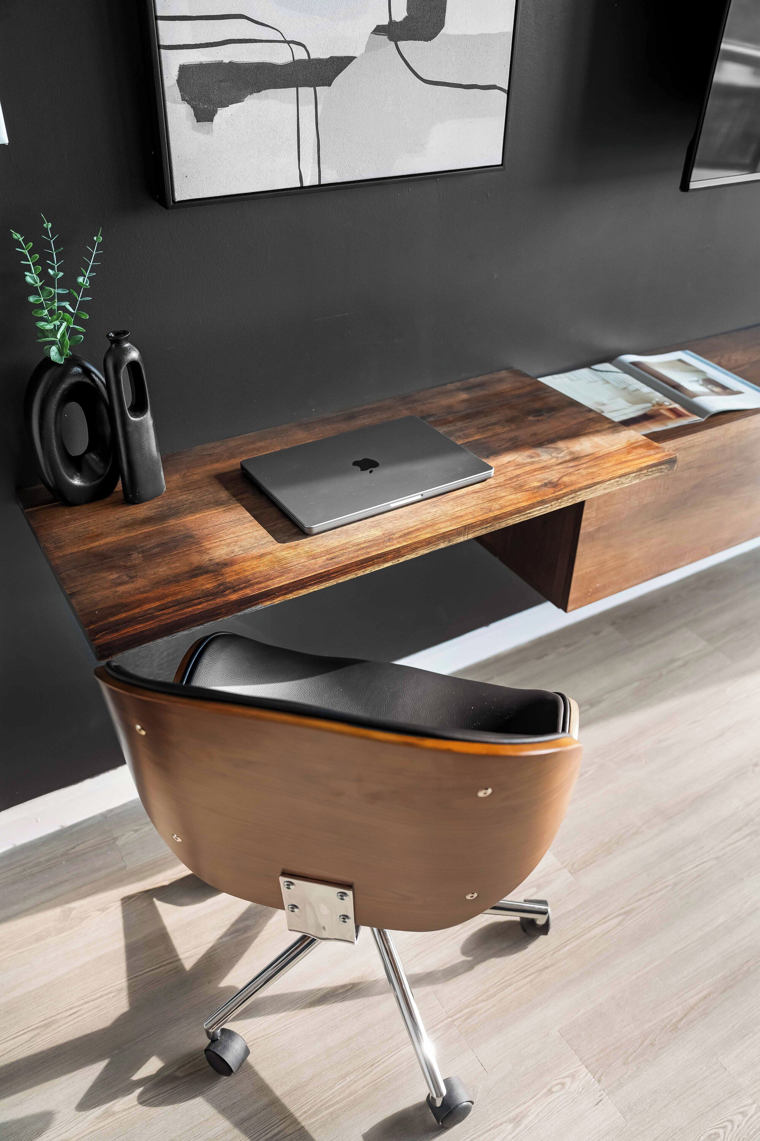 A modern office chair with wheels, a wooden desk with a laptop, and a small plant.
