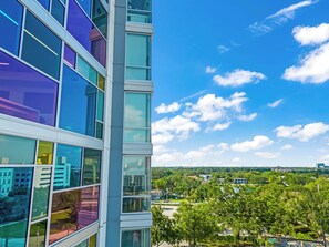 A modern building with large windows and a view of a green landscape. - The Maximus 1BR - King Bed, Rooftop Pool, Gym (Orlando)