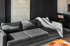 Ein modernes Wohnzimmer mit einem grauen Sofa, einer weißen Decke und einem Holztisch mit einem Buch und Trauben.