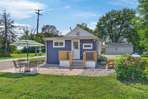 A small single-story house with a front porch, a patio table and chairs, and a covered outdoor seating area.