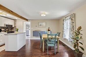 Eine moderne Küche mit einer zentralen Kochinsel, einem Essbereich mit Holztisch und Stühlen sowie einem großen Fenster mit Vorhängen.