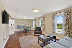 Ein Wohnzimmer mit Sofa, Couchtisch, Wandfernseher, Essbereich mit Tisch und Stühlen sowie einer Küche im Hintergrund.